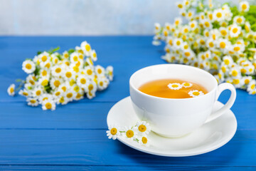Fototapeta na wymiar Chamomile tea on a blue table. Delicious tonic, soothing and relaxing chamomile tea with chamomile flowers, honey and lemon. Herbal tea for immunity. Close-up.Place for text.Copy space.