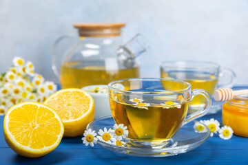 Chamomile tea on a blue table. Delicious tonic, soothing and relaxing chamomile tea with chamomile flowers, honey and lemon. Herbal tea for immunity. Close-up.Place for text.Copy space.