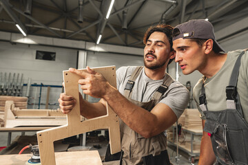 Two young men carpenters making furniture in warehouse of wood factory