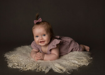 adorable baby girl with precious smile doing tummy time on wool blanket with bow and pink romper dress