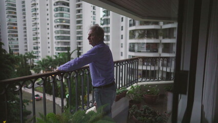 One pensive senior man standing at apartment balcony looking out. Contemplative male 70s person...