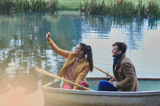 Young woman taking selfie while in row boat with her boyfriend.