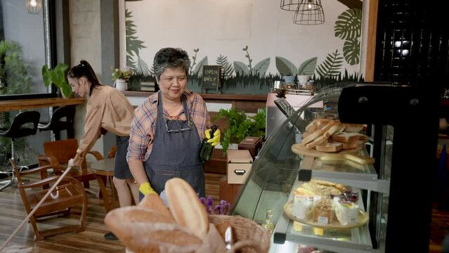 Two Asian women who are mother and son, they are helping clean their own cafe bakery, which is family business, mother is helping daughter clean store after store has closed for customer orders.