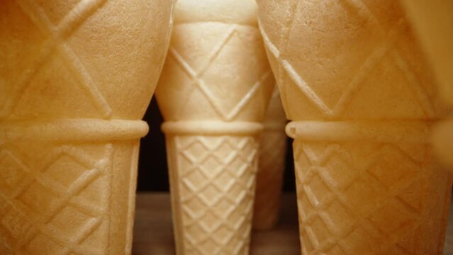 Empty waffle ice cream cones are lined up in a row on the table against a black background. The camera glides through them.