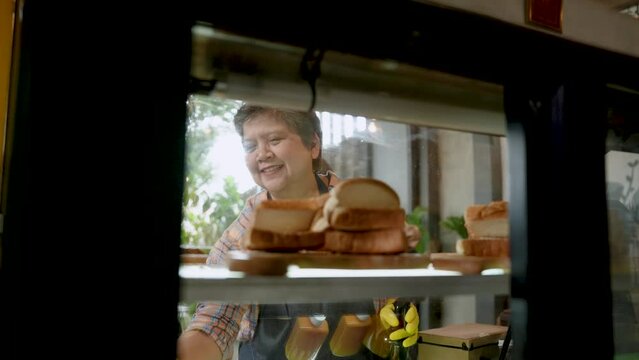 Portrait, face Asian mother is mother cafe owner, is using cloth spraying water from spray bottle onto glass cabinet, wipe clean bakery cabinet always clean, mother has good mood, does not feel tired.
