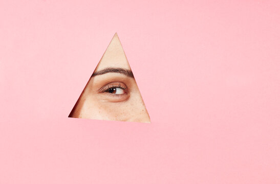 Young woman peeking through cutout in pink paper