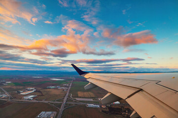 Airplane flight in sunset sky over city and wing of plane. View from the window of the Aircraft. Traveling in air.