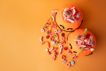 Baskets in the form of pumpkins with sweets on an orange background.