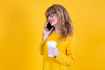 woman talking on smartphone and with takeaway drink on yellow background