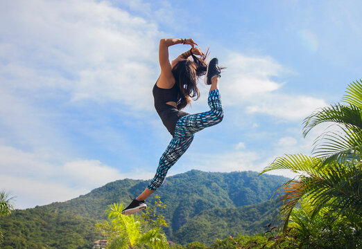 Young woman in yoga pants jumping by mountain