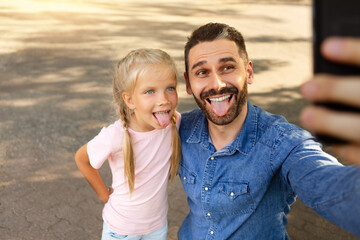 Funny middle aged father walking with his little daughter outdoors in park, making selfie and...