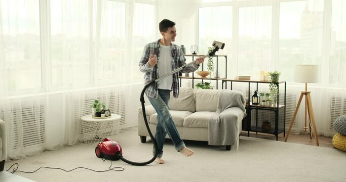 Young and active Caucasian individual is seen dancing while cleaning in the living room. With high spirits and infectious energy, he effortlessly combines household chores with passion for dancing.