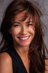 Close-up portrait of a beautiful brunette haired woman cheerful smiling against grey bacgkround
