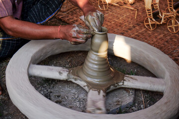 Hands of a Potter is shaping clay pot using his wheel 