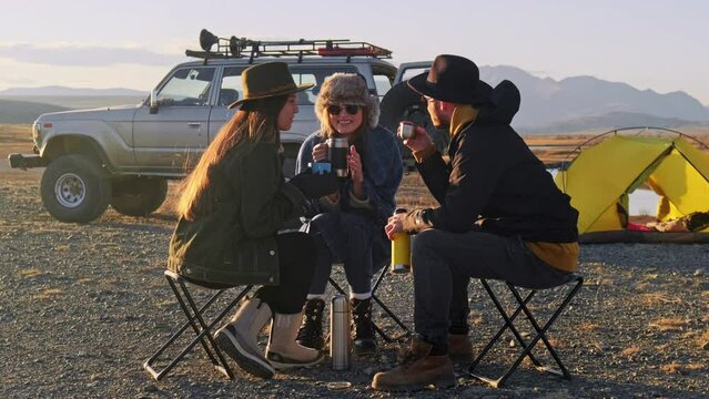Group of Friends reparing coffee near travel suv. People enjoying a day camping. Autumn vacations and relationship concept. Picnic near car on sunset outside. Domestic travel concept.