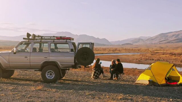 Group of Friends reparing coffee near travel suv. People enjoying a day camping. Autumn vacations and relationship concept. Picnic near car on sunset outside. Domestic travel concept.