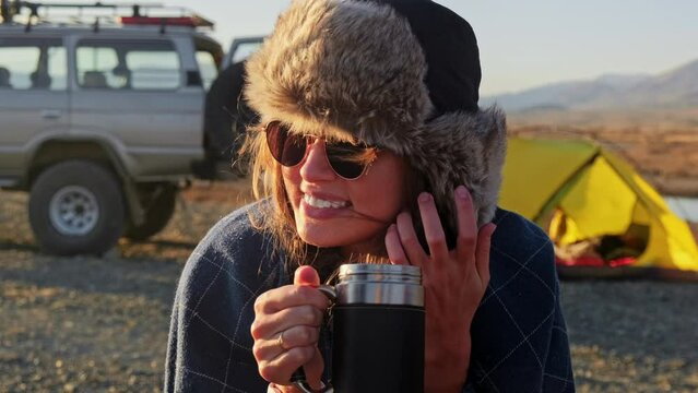 Happy woman holds a cup and drinks coffee near travel suv. People enjoying a day camping. Autumn vacations and relationship concept. Domestic travel concept.