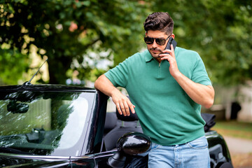 Handsome man standing next to his convertible car and using smartphone