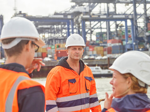 Dock manager and supervisor instructing worker to move cargo containers infront of ship