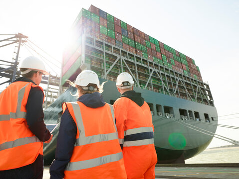 Managers communicating by dockside infront of cargo ship and cranes