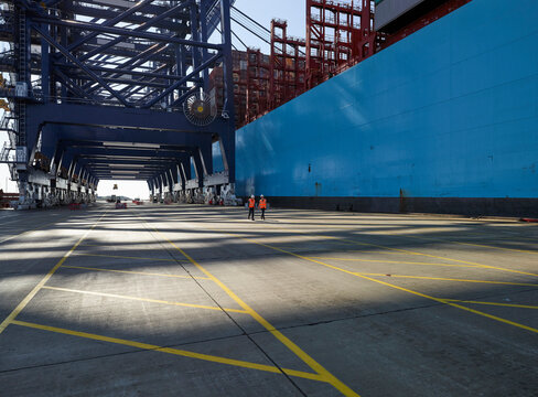 Dock workers next to blue container ship, Felixstowe, England.