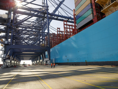 Two dock workers walking alongside cargo container ship, Felixstowe, England.