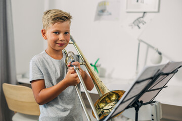 A Caucasian boy is holding a trombone.