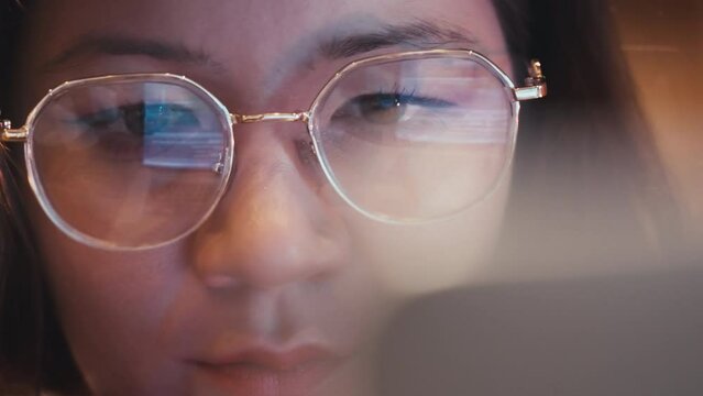 Female asian person working at a computer. Close-up freelancer wearing glasses reflecting screen of laptop with cartoon. Designer drawing. Asian woman creating illustration. IT professions.