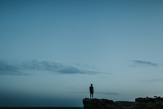 Silhouette of a young man on rocks at Calo des Moro in Mallorca - Powered by Adobe