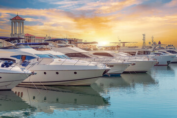 The blue water reflects orange sunset sky. Rows of sailing yachts, motor boats and fishing boats....