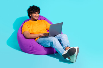 Full body photo of young relaxed man lying pouf netbook browsing his google search history find password isolated on cyan color background