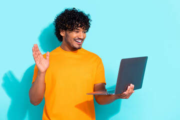 Photo of young man wavy hair wear orange t shirt waving palm hello seminar video call using netbook isolated on aquamarine color background