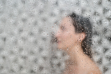 Fototapeta premium woman showering in bathroom interior, view through the glass with water vapor and drops