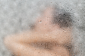 woman showering in bathroom interior, view through the glass with water vapor and drops