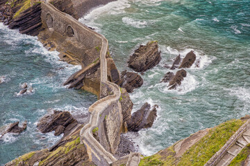 view of the rocky bridge to gaztelugatxe island in stormy weather and high surf