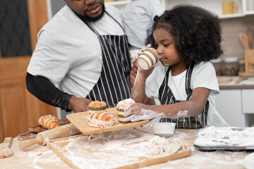 Happy African American kid girl and father cooking break or bakery at kitchen at home	