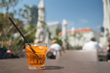 A cold drink with straw and ice cubes on a hot day in the beer garden - obrazy, fototapety, plakaty