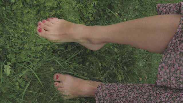 vertical video a girl in a long dress walks barefoot on the green grass in summer, the theme is relaxation. High quality 4k footage
