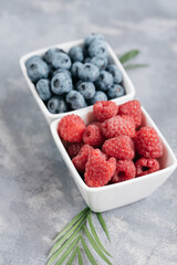 Top view on fresh pile of blueberries and raspberries in white square bowl on grey background. Healthy eating. Vegan food