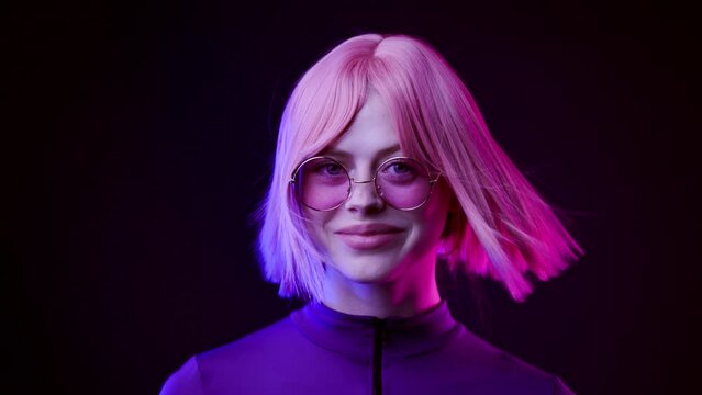 Beautiful woman in futuristic costume over dark background. Violet neon light. Girl in glasses smiling and looking at the camera.
