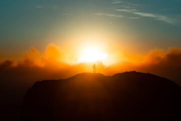 Woman standing in front of sun on mountain side rocks