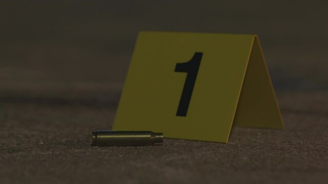 A crime scene evidence marker place next to a bullet casing shell on a sidewalk at night gun crime violence