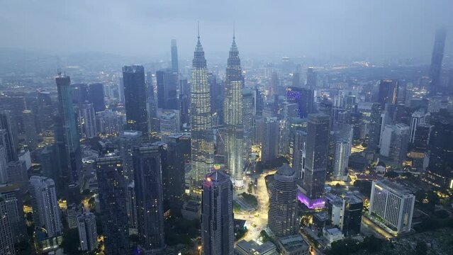 Aerial drone video of Kuala Lumpur City Center and the Petronas Towers in the early morning with a blue haze over the city and some lights on