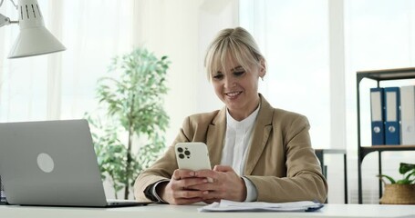 A Caucasian woman casually checking her phone while in her office. Her actions convey everyday moments as she browses through messages or updates. The office atmosphere exudes a sense of calmness.