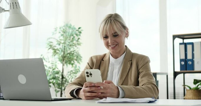 A Caucasian woman casually checking her phone while in her office. Her actions convey everyday moments as she browses through messages or updates. The office atmosphere exudes a sense of calmness.