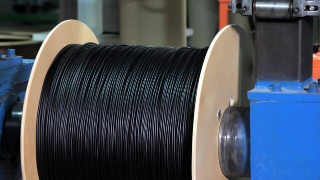 Winding of the optical cable to the bobbin in the production line. Cable pdroduction. Cable factory. Winding the black cable onto the reel. Production line at factory for production of Internet wire
