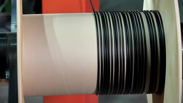 Winding of the optical cable to the bobbin in the production line. Cable pdroduction. Cable factory. Winding the black cable onto the reel. Production line at factory for production of Internet wire