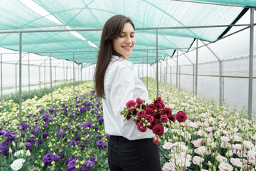 Businesswoman holds a beautiful bouquet in the green house. Woman portrait with flowers. Female florist has an order for fresh flowers.