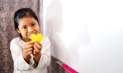 Niña latina sonriente y feliz sosteniendo en sus manos un corazón de papel. Concepto de amor,...