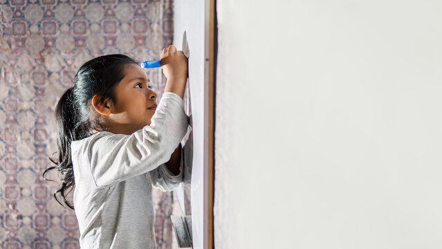 Ni&ntilde;a latina sonriente y feliz, escribiendo en la pizarra de clases con plumones de colores. Espacio para texto.